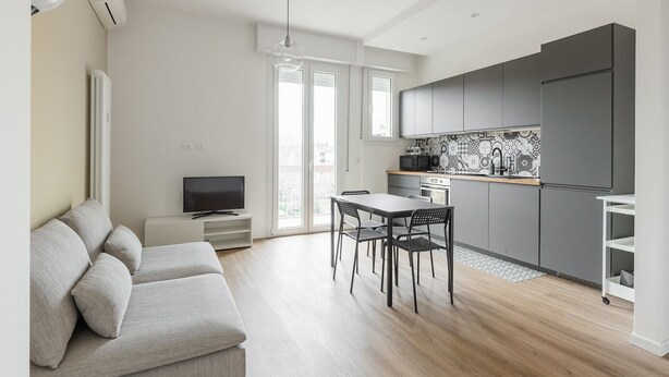 A modern kitchen with grey cabinets, a dining area with a table and chairs, a flat-screen TV on a stand, and a sofa in the living area. - Casa Amarenzi by Wonderful Italy (Bologna)