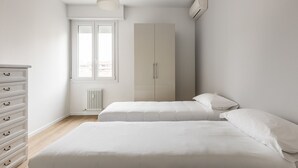 A minimalist bedroom with two beds, a dresser, a radiator, and a window with blinds. - Casa Amarenzi by Wonderful Italy (Bologna)