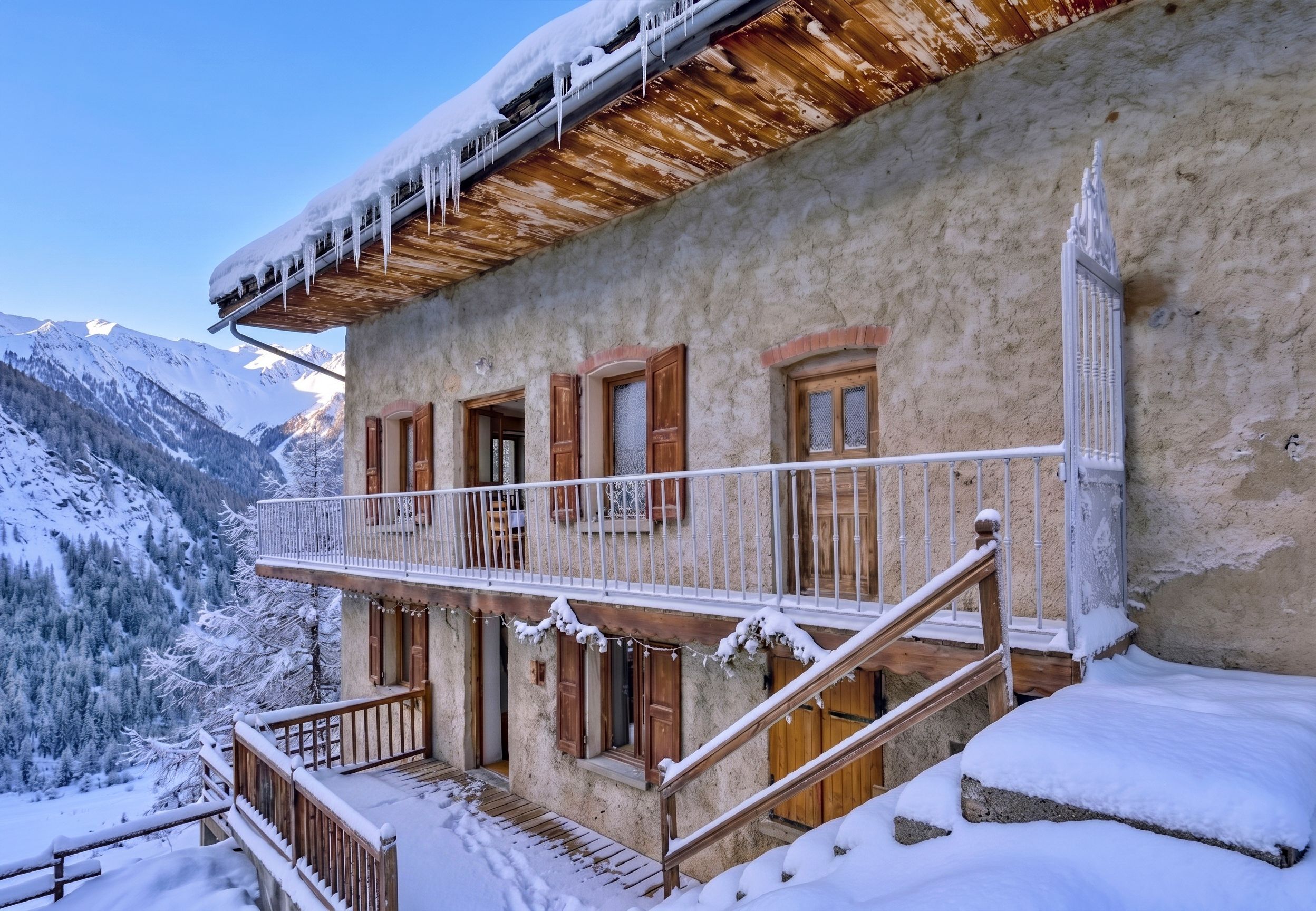 A snow-covered building with a balcony, wooden railings, and a staircase leading to the entrance.