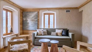 A cozy room with a wooden ceiling, a sofa with cushions, a small round table, and a radiator. - CASA-Niu Luxe discret, vue et pied des pistes (Molines-en-Queyras)