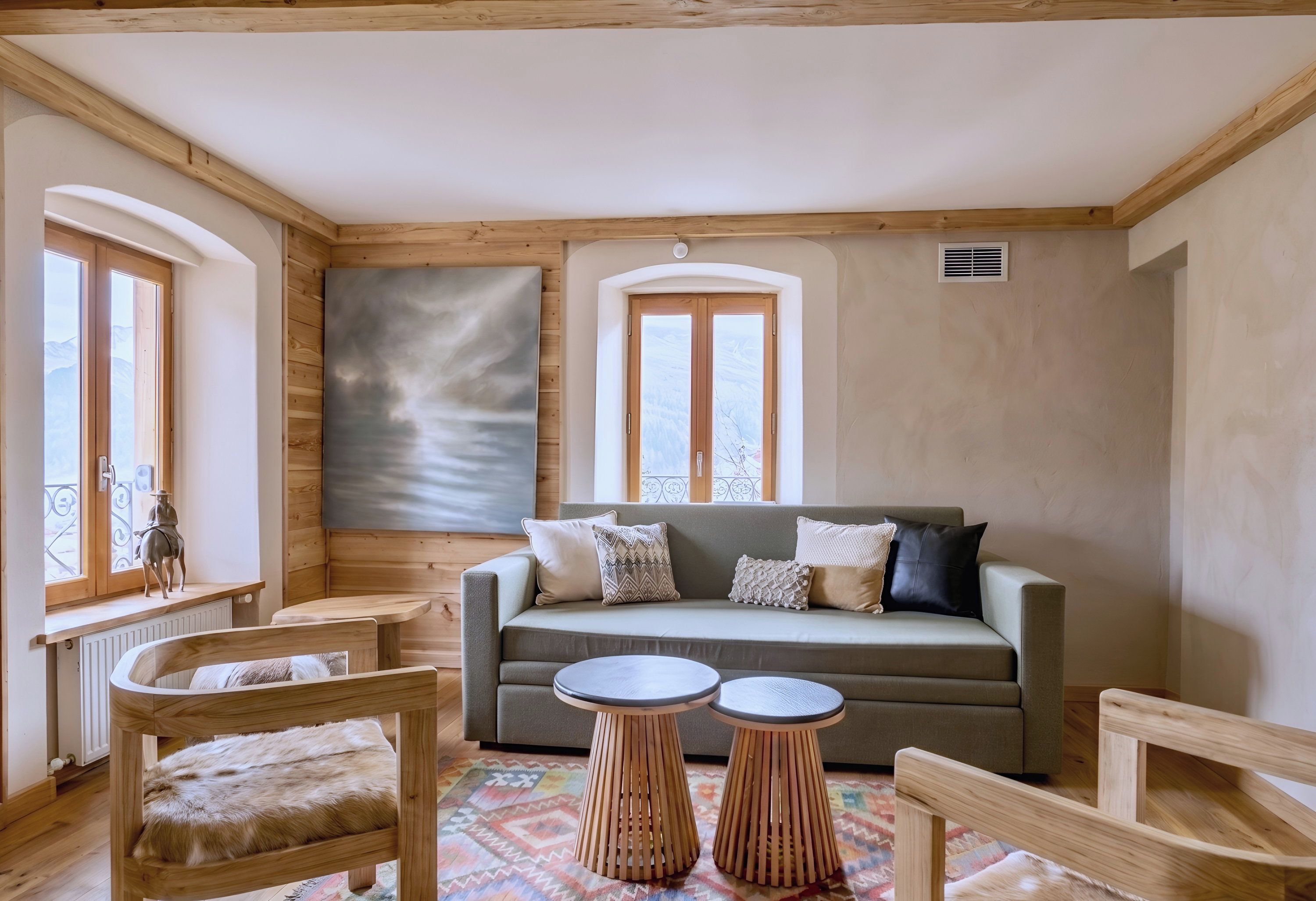 Ein gemütliches Zimmer mit einer Couch, zwei runden Holztischen und einem Sessel mit einem Fellüberwurf.