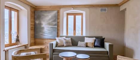 Een gezellige kamer met een bank, twee ronde houten tafels en een stoel met een bont plaid.