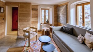 A cozy room with wooden walls, a red door, a sofa, a small table, and a window with a view of houses. - CASA-Niu Luxe discret, vue et pied des pistes (Molines-en-Queyras)