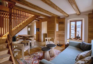 Ein Holzinnenraum mit Treppe, einer Couch, einem Esstisch und Blick durch ein Fenster.