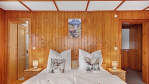 A wooden-paneled room with a bed, two nightstands, and a painting of a mountain scene.