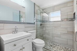 A modern bathroom with a glass shower enclosure, a white sink, and a toilet. - La Maison Bleue (New Smyrna Beach)