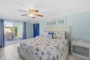 A bedroom with a bed, a nightstand, a ceiling fan, and a view of the outdoors. - La Maison Bleue (New Smyrna Beach)