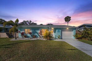 A residential house with a well-maintained lawn, a garage, and a variety of plants. - La Maison Bleue (New Smyrna Beach)