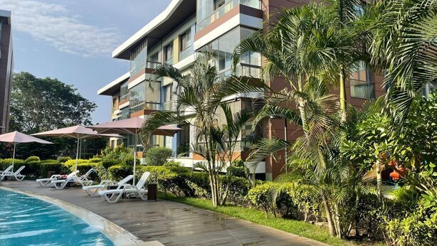 A modern hotel with a swimming pool, lounge chairs, and palm trees. - Peravi Suites at Pearl In The City (Accra)