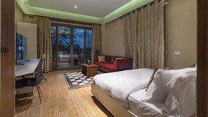 A modern hotel room with a large bed, a desk, and a sofa. There is a view of the outdoors through the glass door. - Peravi Suites at Pearl In The City (Accra)