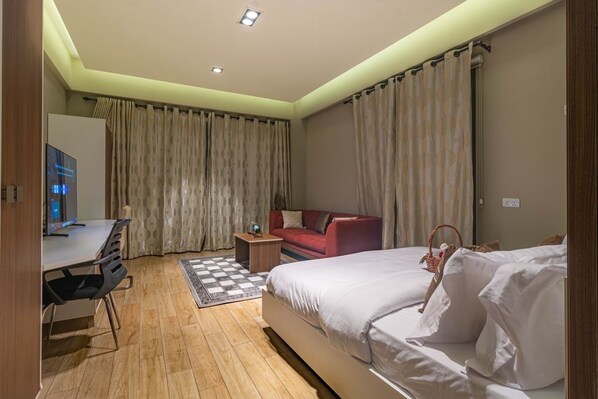 A hotel room with a bed, a desk, a red sofa, and a TV. - Peravi Suites at Pearl In The City (Accra)