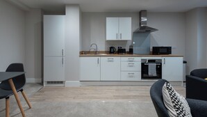 A modern kitchen with white cabinets, a stainless steel range hood, and a microwave. There is a dining area with a black table and chairs. - Chic 1Bed in Hull City Centre near Hull College (Hull)