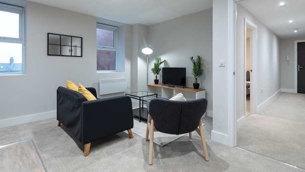 A modern living room with a black sofa, a grey armchair, a glass coffee table, and a flat-screen TV on a wooden stand. - Chic 1Bed in Hull City Centre near Hull College (Hull)