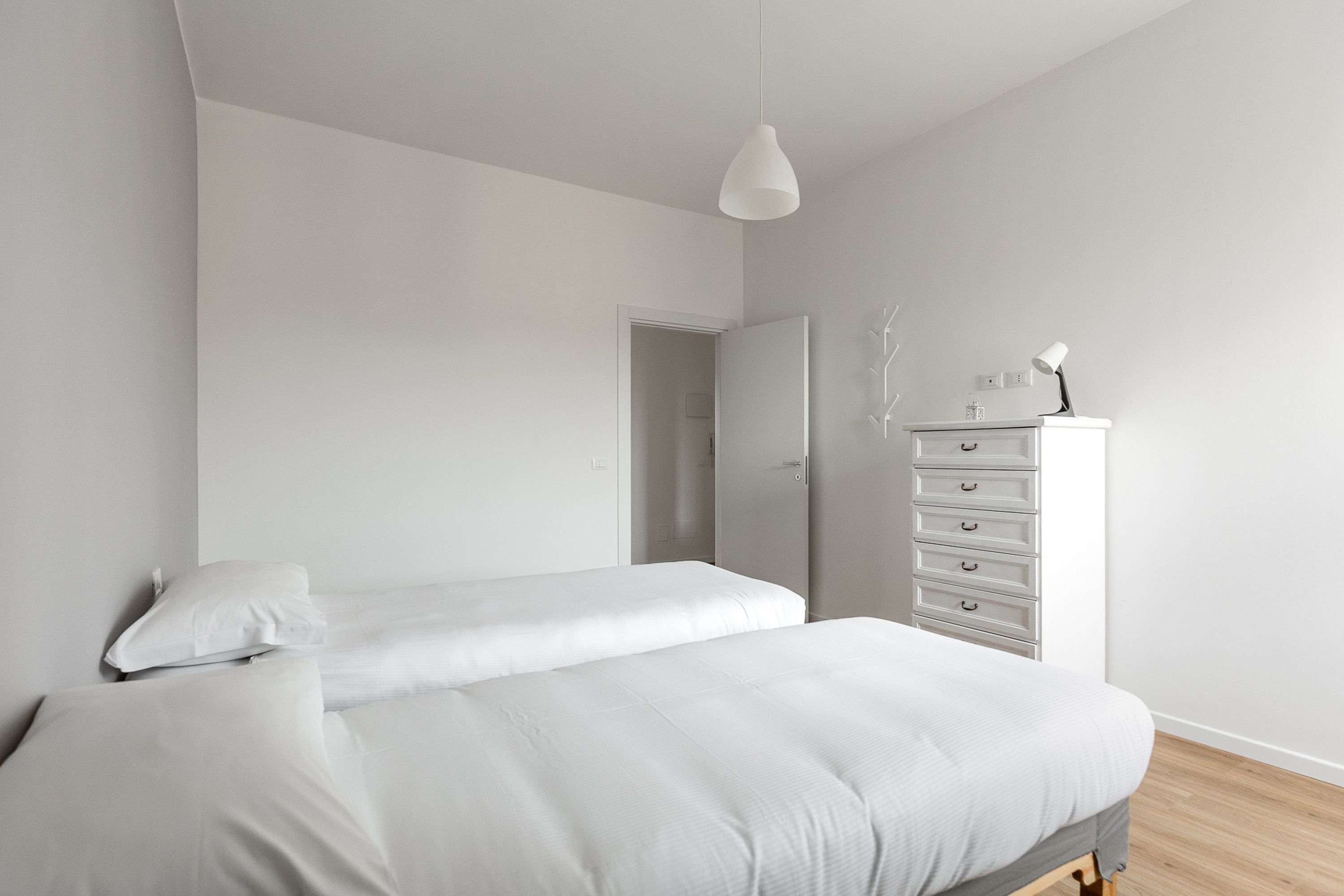 Un dormitorio minimalista con dos camas, un aparador y una lámpara colgante.