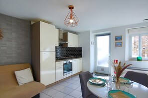 Een moderne keuken met witte kasten, een zwart betegelde spatwand en een eetgedeelte met een tafel voor twee personen.