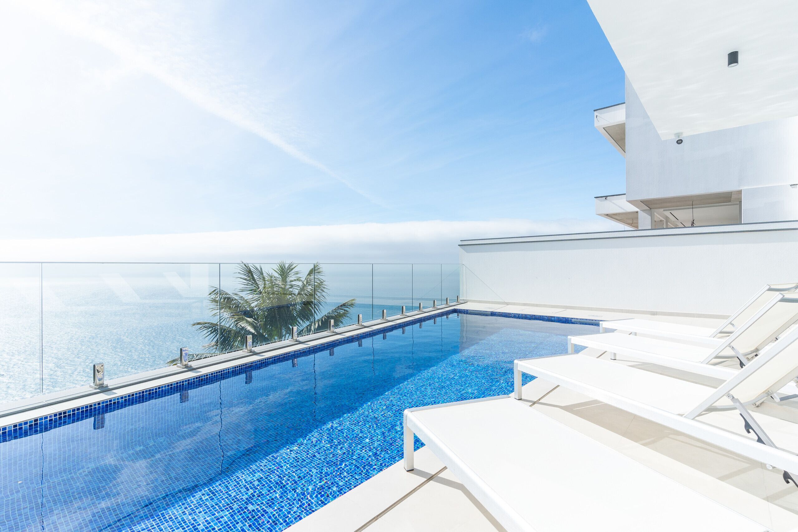 Una piscina moderna d'hidromassatge infinit amb aigua blava cristal·lina, gandules blanques i vistes a l'oceà.