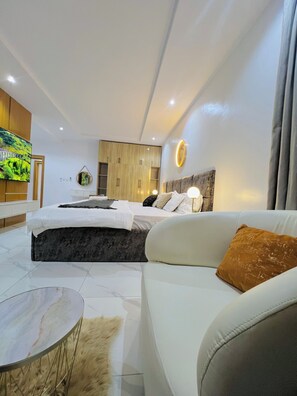 Une chambre moderne avec un grand lit, un canapé, une télévision et une armoire en bois.