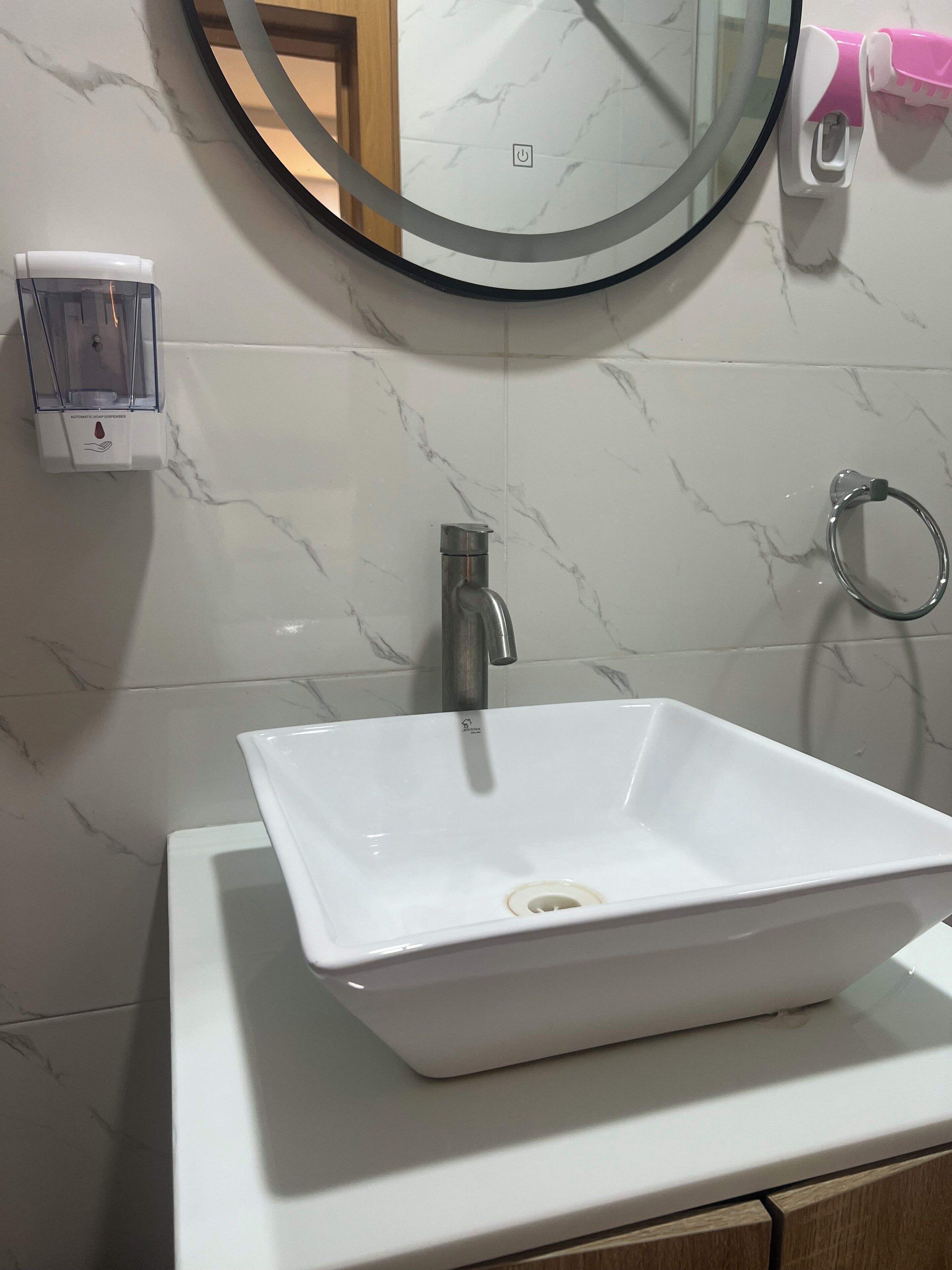A bathroom with a white sink, a round mirror, and a soap dispenser.