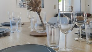 A dining table set with clear glassware and plates, a decorative plant, and a painting on the wall. - Seaside Cottage - Le Coquelicot (Pirou)
