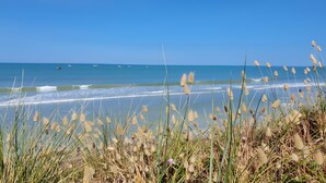 A beach with waves, grass, and a clear sky. - Seaside Cottage - Le Coquelicot (Pirou)