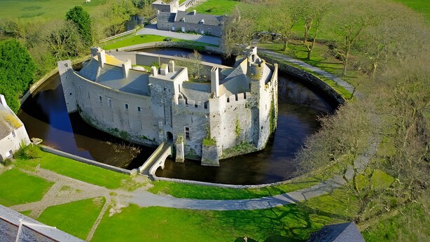 A castle with a moat, a bridge, and a small building to the left. - Seaside Cottage - Le Coquelicot (Pirou)