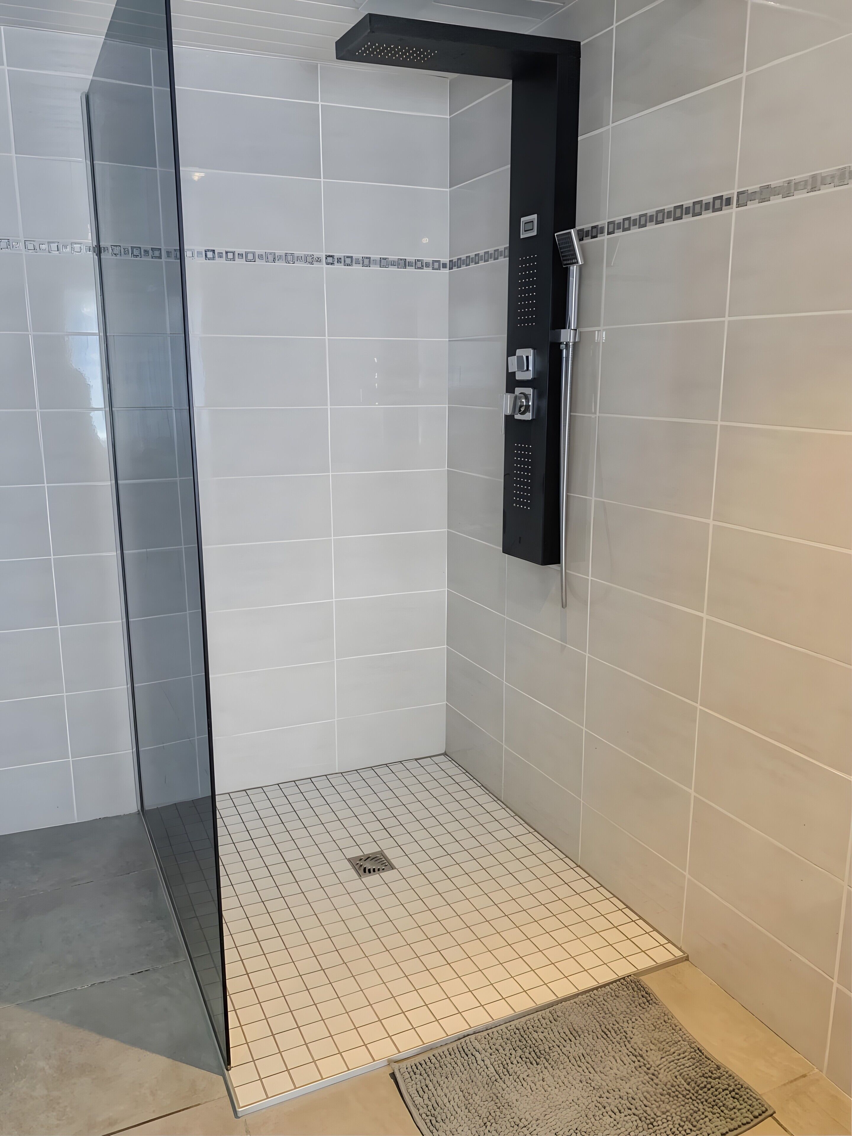 Une douche avec une porte en verre, un panneau de commande et un sol carrelé.