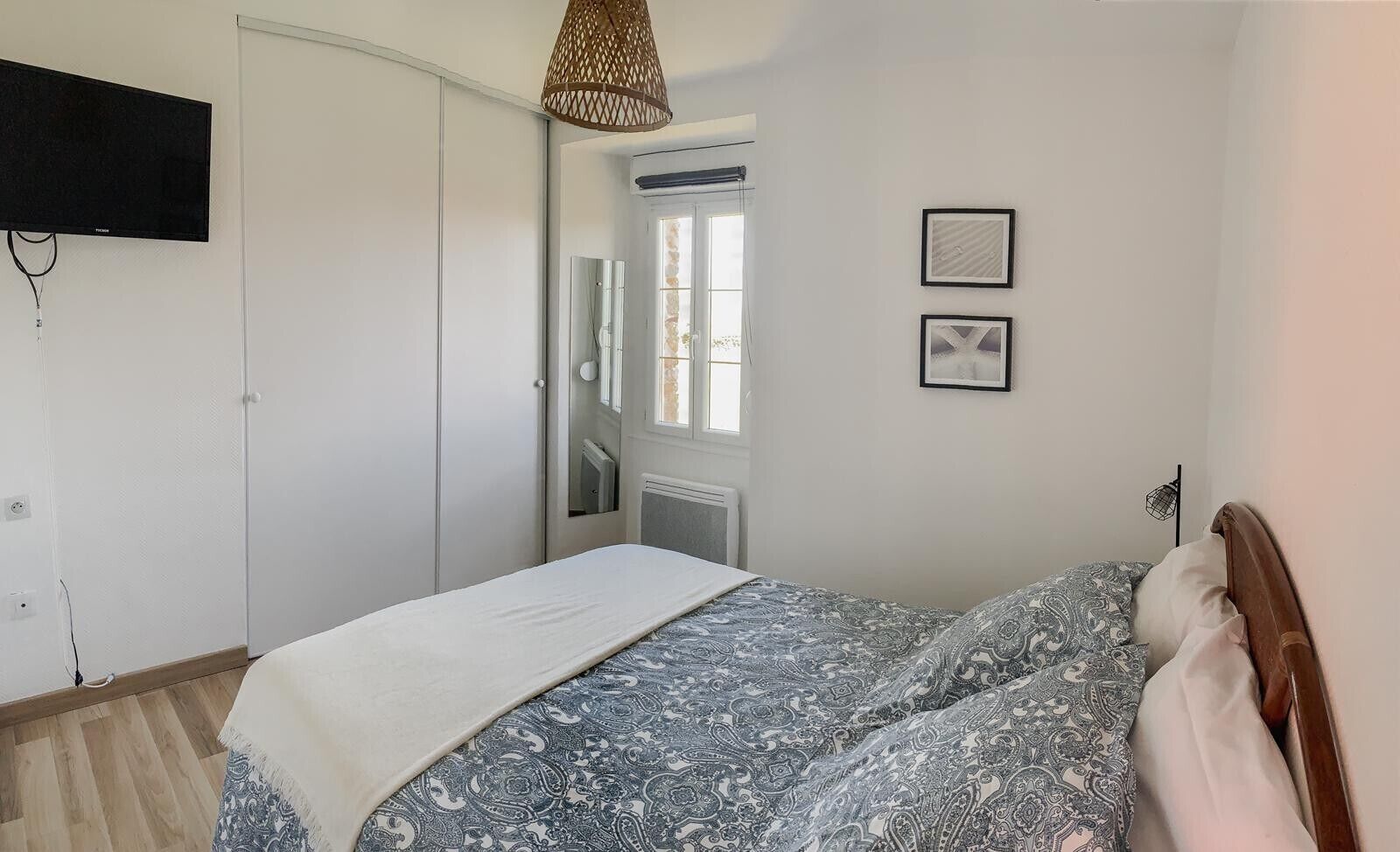 Quarto com cama, guarda-roupa, televisão na parede e janela com cortinas.