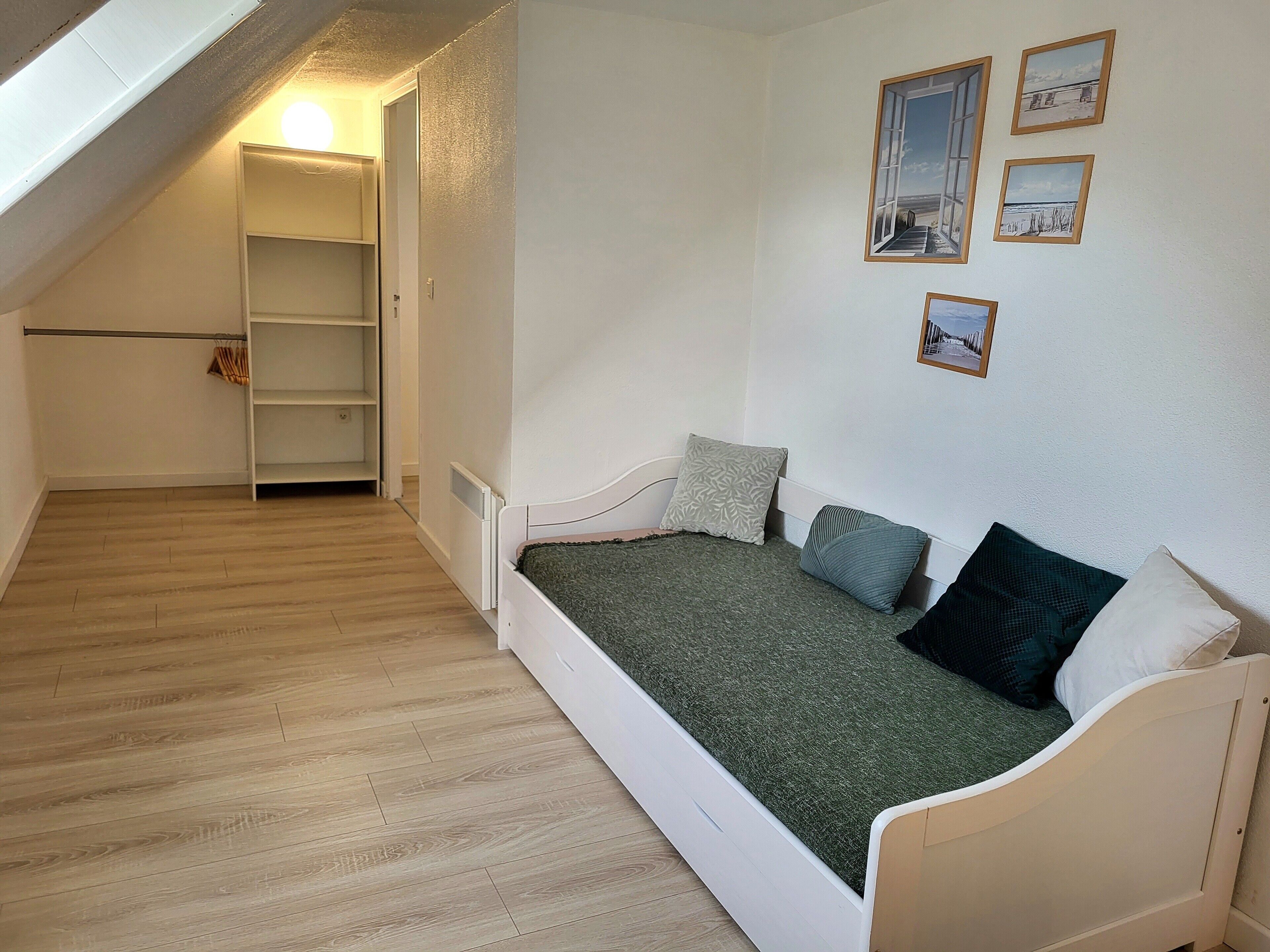 Een kleine kamer met een enkel bed, schuine wand, inbouwkast en een radiator.