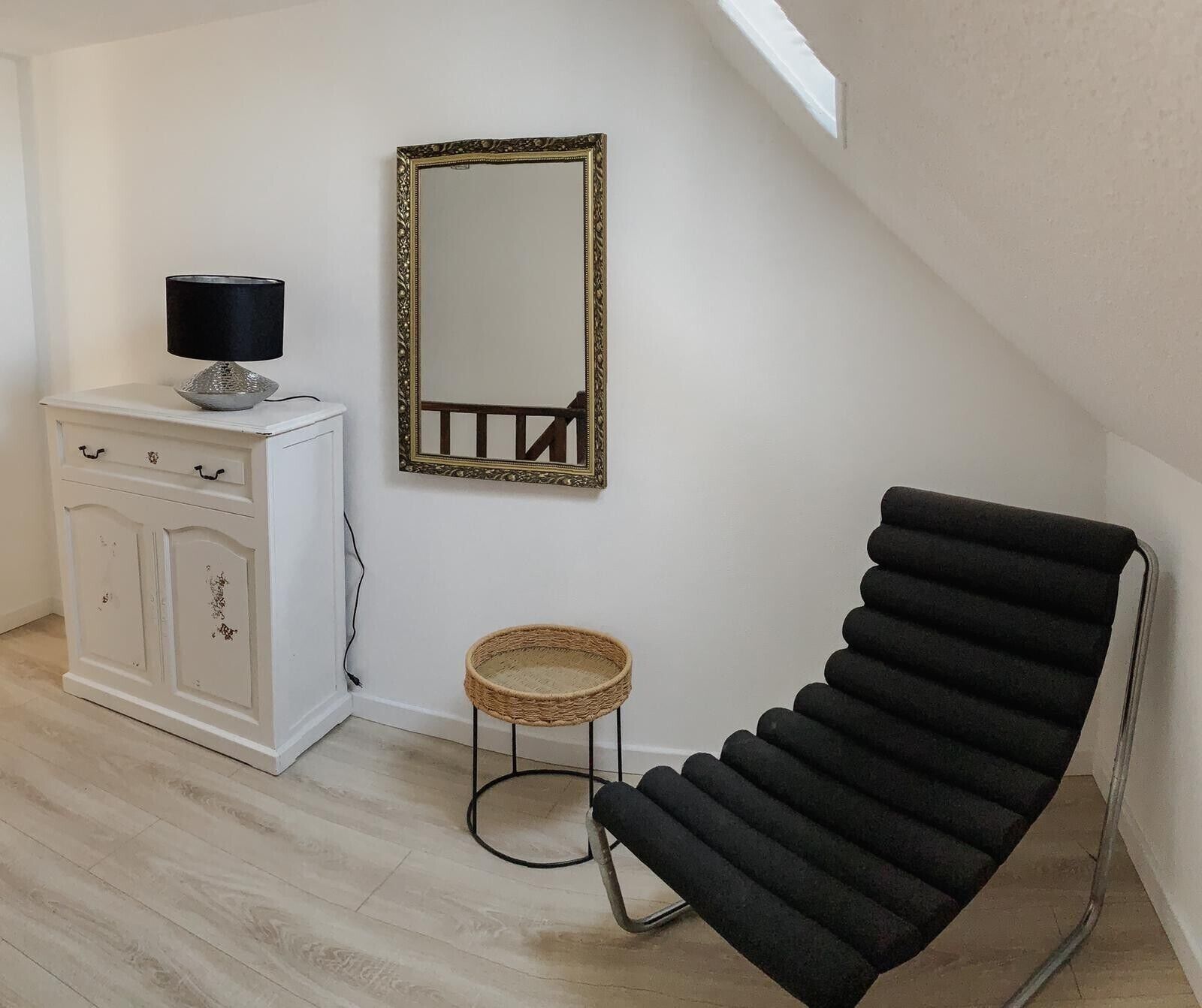 Quarto com um armário branco, uma cadeira preta, uma mesa redonda pequena e um espelho na parede.