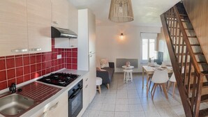 Eine moderne Küche mit Gasherd, integriertem Backofen und einer roten Küchenrückwand. Ein Essbereich mit Tisch und Stühlen sowie eine Holztreppe sind ebenfalls vorhanden.