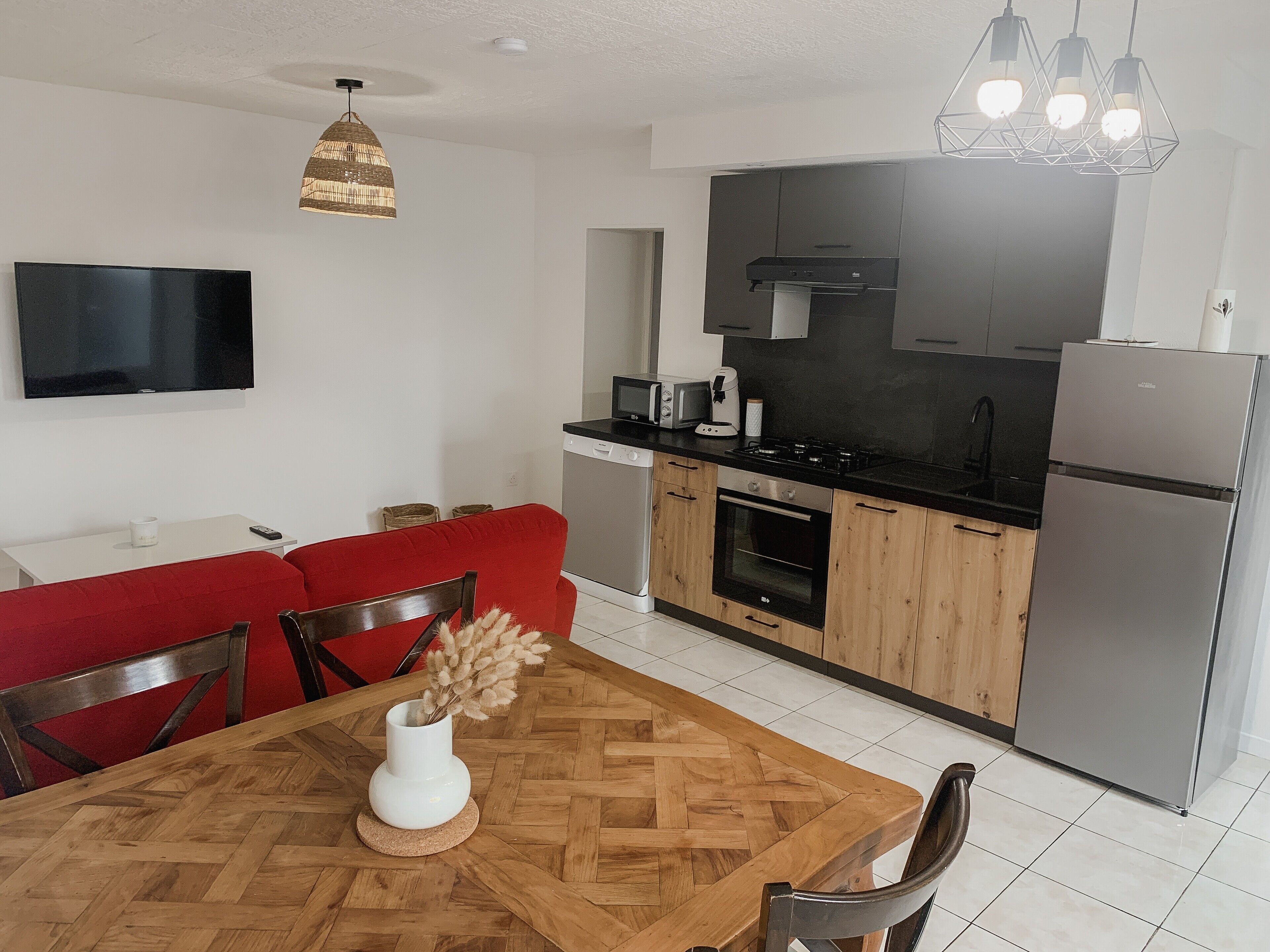 A modern kitchen with a dining area, including a TV, sofa, and a table with a vase.