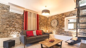 A modern living room with a stone wall, a grey sofa with red cushions, a wooden coffee table, and a black ottoman. - A Casinha by Atlantic Holiday (Câmara de Lobos)
