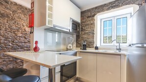 A compact kitchen with a stone wall, a microwave, a coffee maker, and a window with a view. - A Casinha by Atlantic Holiday (Câmara de Lobos)