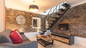 A modern living room with a stone wall, a staircase, a sofa, a coffee table, and a TV mounted on the wall. - A Casinha by Atlantic Holiday (Câmara de Lobos)