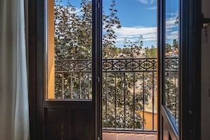 Un balcone con ringhiera in ferro battuto, vista su alberi e cielo sereno.