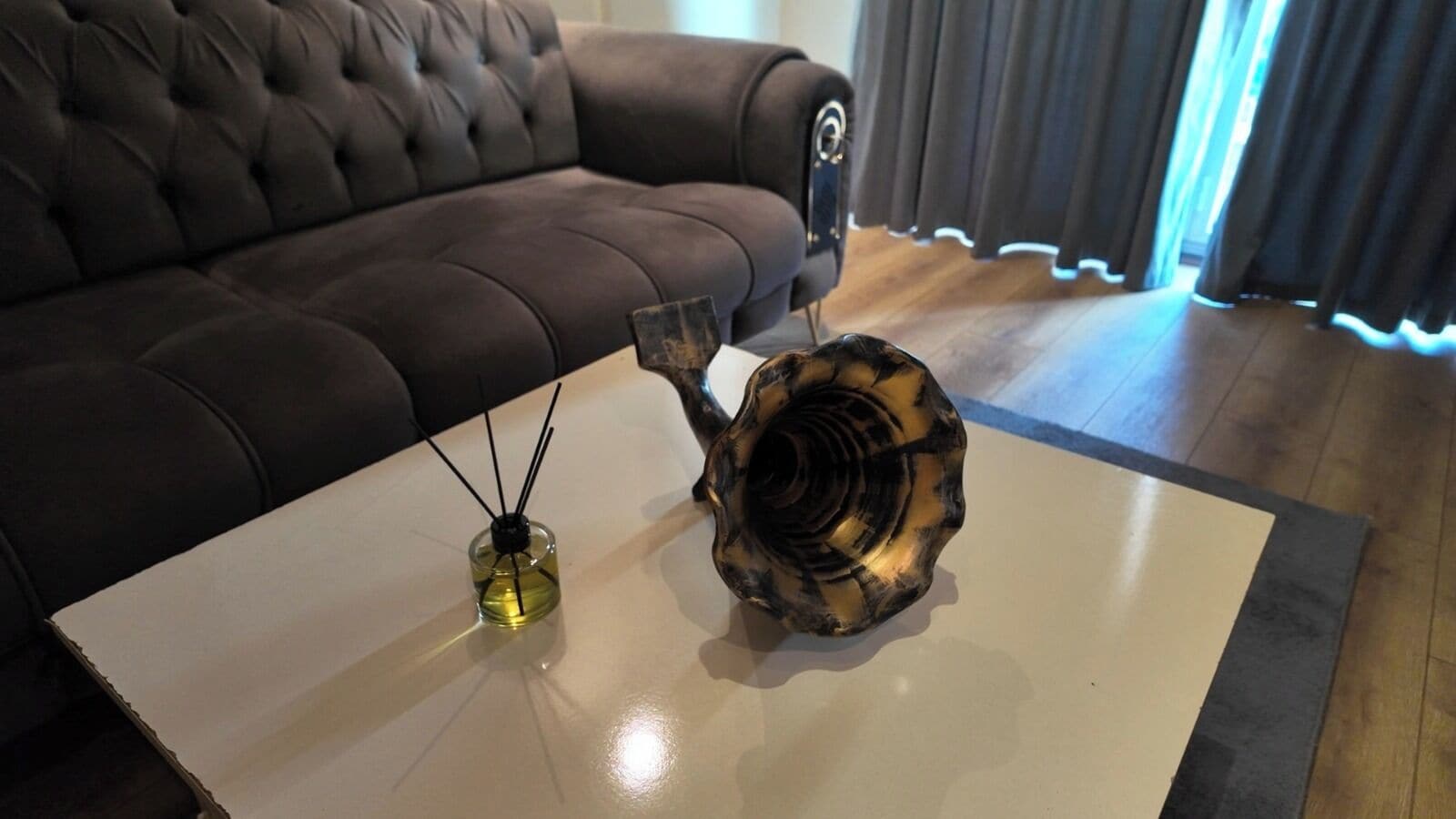 Een woonkamer met een bruine bank, een witte salontafel en een decoratieve schelp.