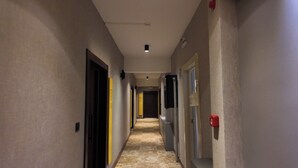 Un corridoio stretto con porte su entrambi i lati, un rilevatore di fumo a destra e un lampadario al soffitto.