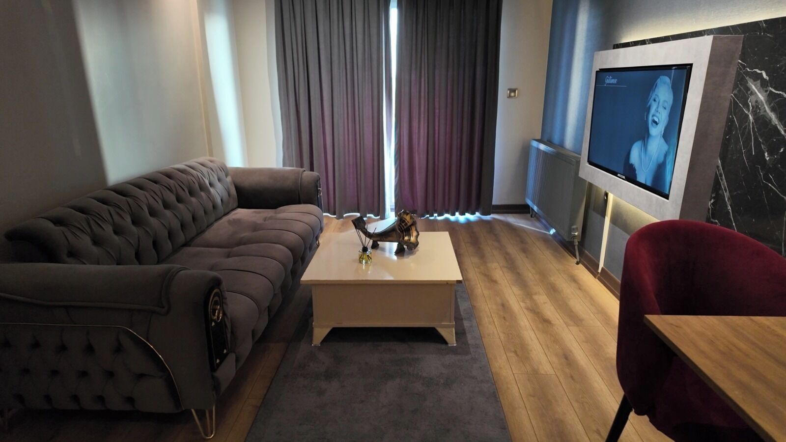 A modern living room with a dark brown sofa, a wooden coffee table, and a red chair. A flat-screen TV is mounted on the wall.