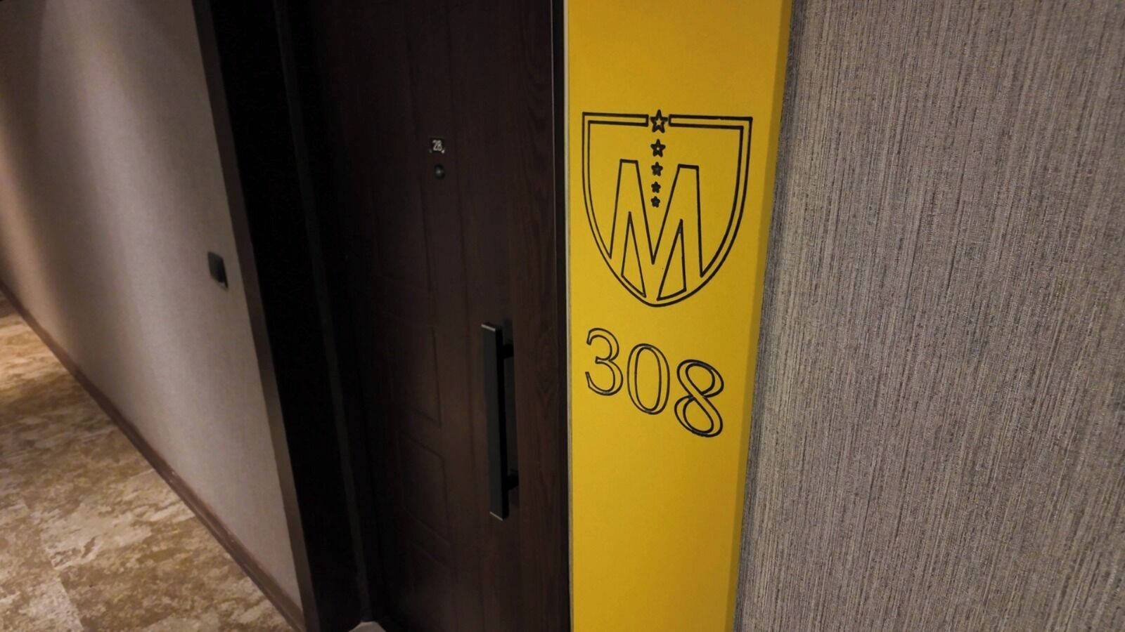 Una puerta con el número "308" y un logotipo sobre una pared amarilla.