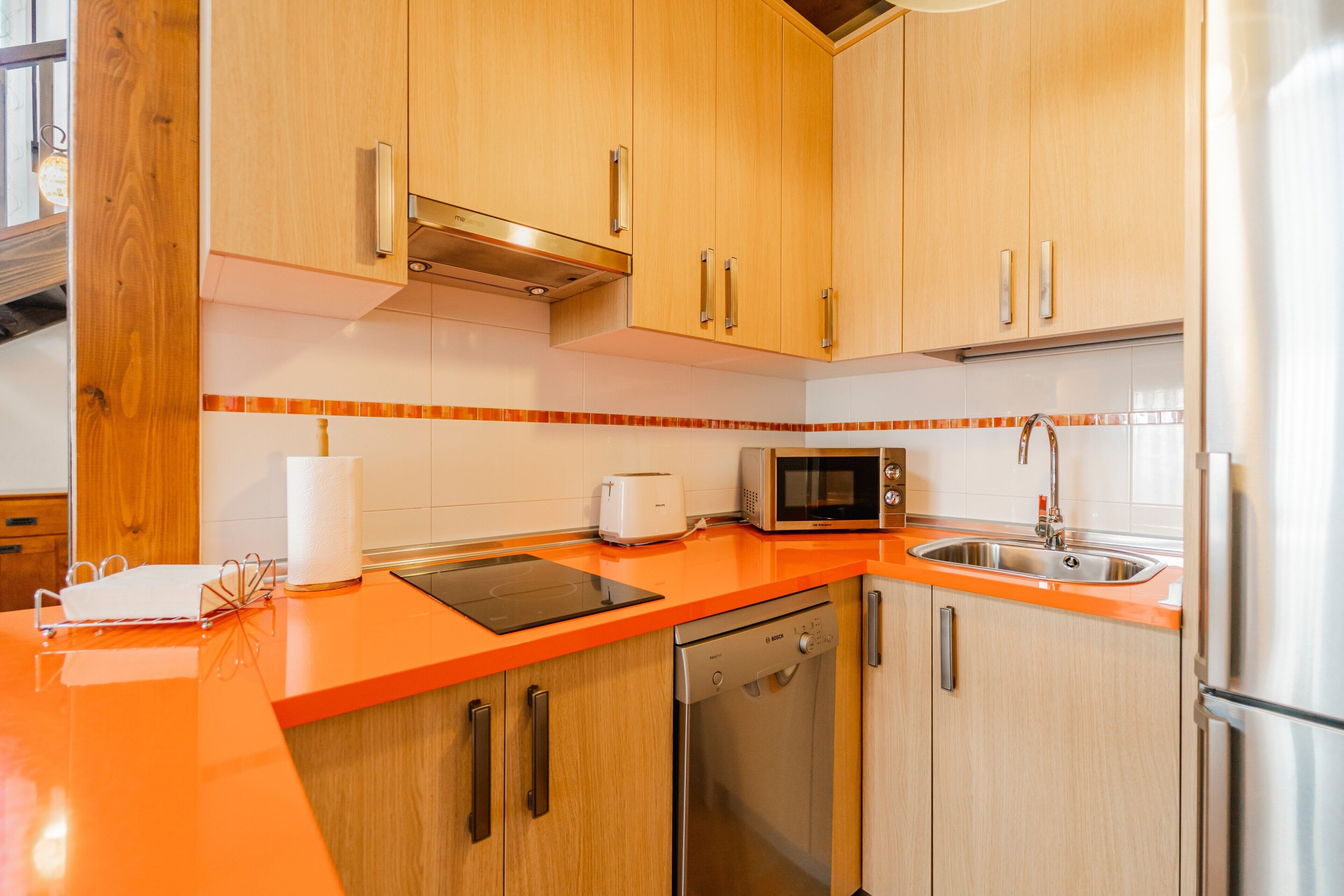 Una cucina con mobili in legno, una lavastoviglie in acciaio inossidabile, un forno a microonde e un lavandino.
