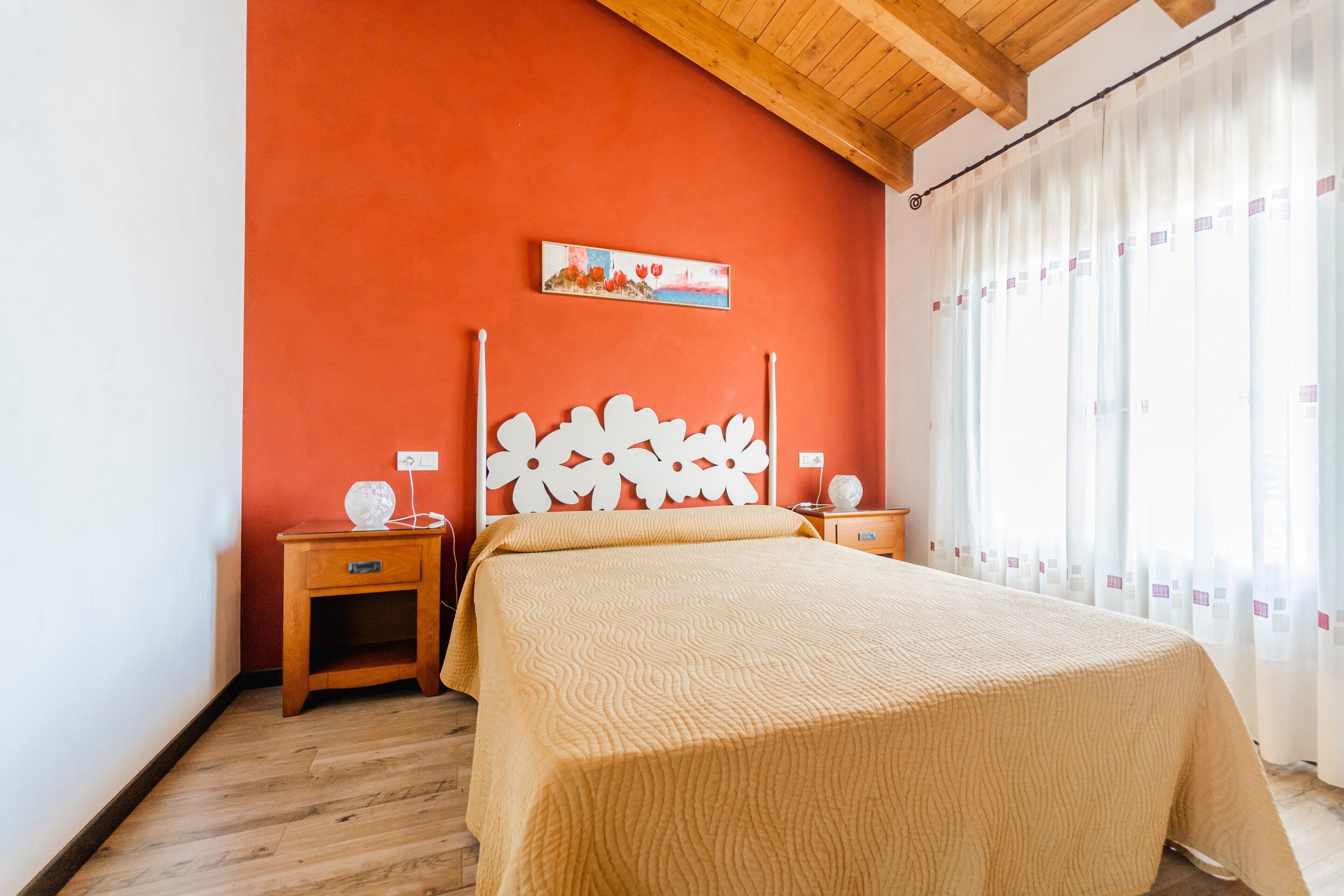 Ein Schlafzimmer mit einem Bett, Holz-Nachttischen, einem an der Wand befestigten Kunstwerk und einem Fenster mit Vorhängen.