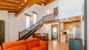 A spacious living area with a wooden staircase, a sofa, a kitchen, and a dining area.