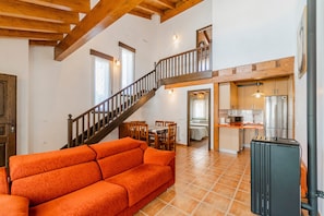 Un'ampia zona giorno con scala in legno, un divano, una cucina e una sala da pranzo.