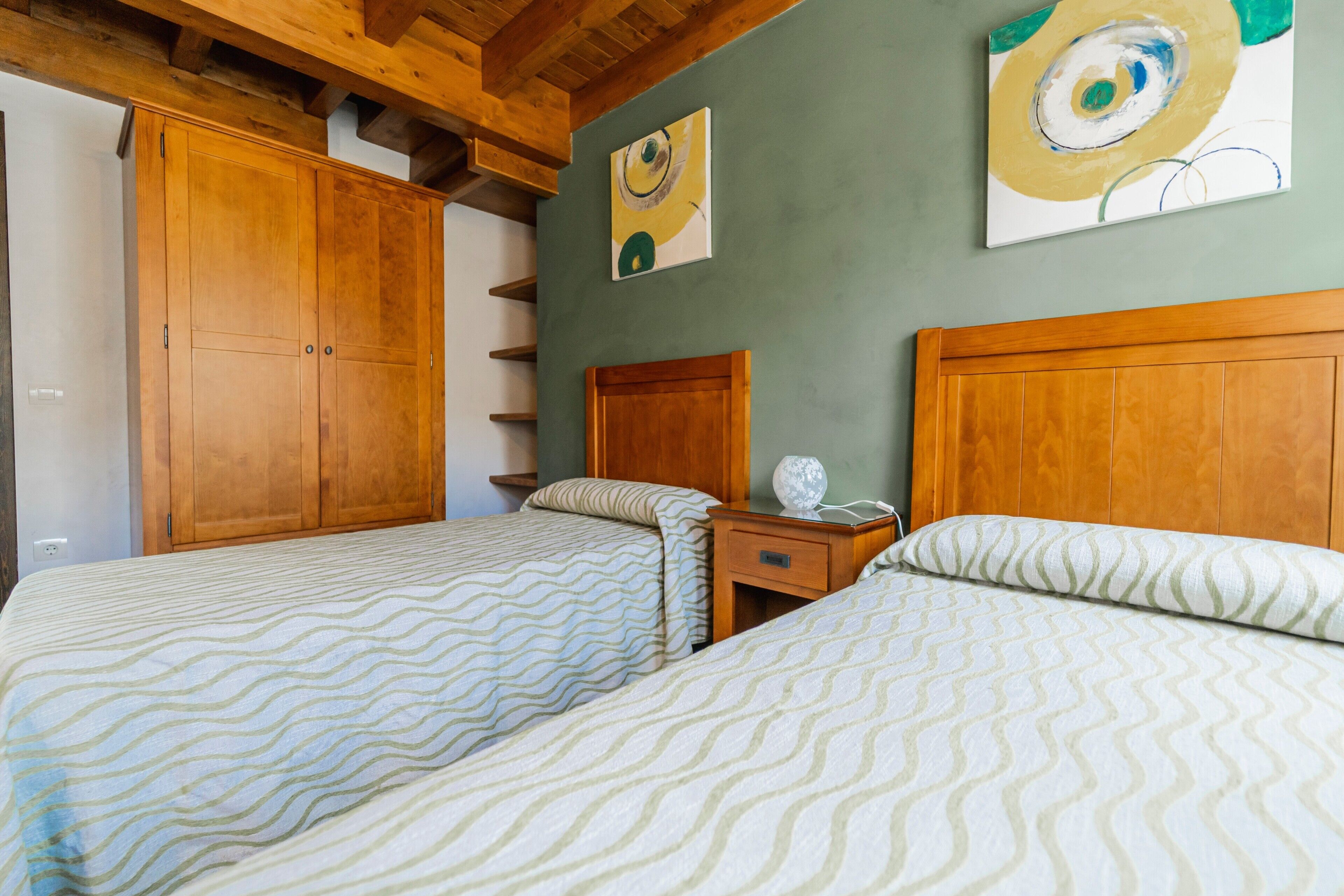 Un dormitorio con dos camas, cabeceros de madera, una mesita de noche y un armario.