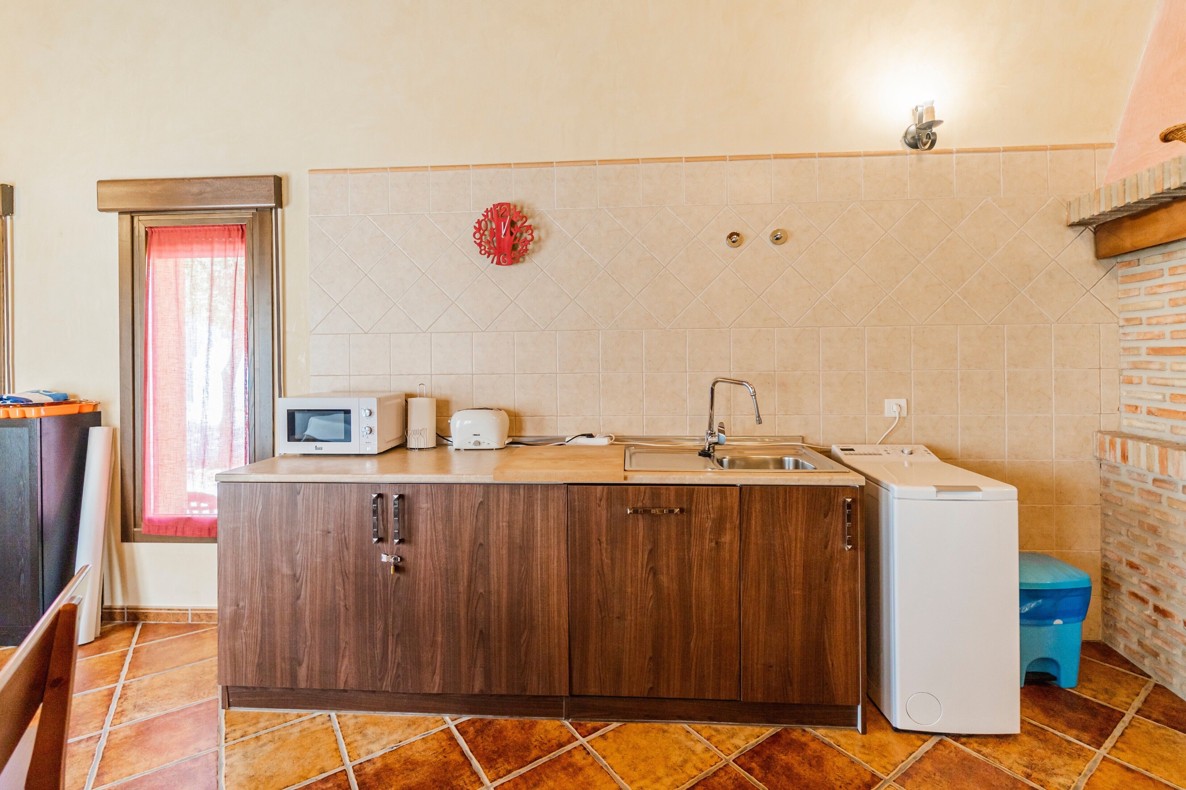 Une cuisine compacte équipée d’un four à micro-ondes, d’un grille-pain et d’un évier, avec des placards en bois et un petit réfrigérateur.