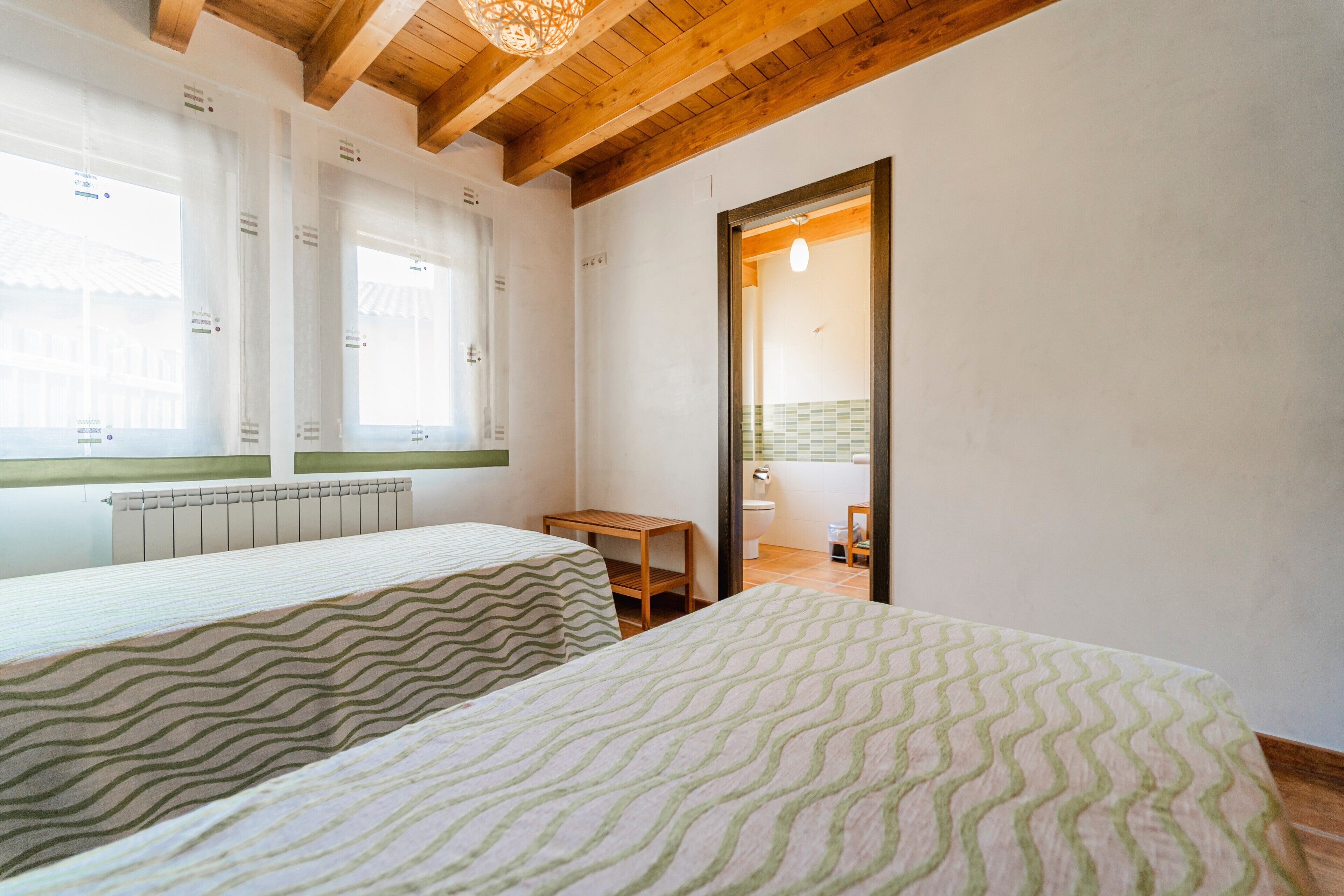 Une chambre avec deux lits, un plafond en bois, une fenêtre et une porte donnant sur une salle de bain.