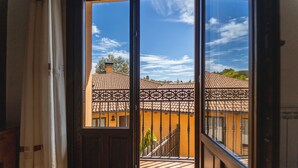 A view through a window with a balcony, featuring a building with a tiled roof and a railing.