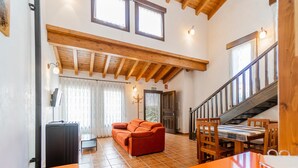 A spacious living area with a sofa, wooden dining table, and a staircase.