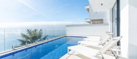 A modern infinity pool with clear blue water, white lounge chairs, and a view of the ocean.