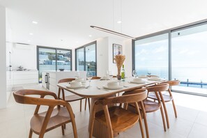 A modern dining area with a white table set for six, surrounded by wooden chairs. - Villa Devaneio by Atlantic Holiday (Ribeira Brava)